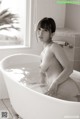 A naked woman sitting in a bathtub in a bathroom.