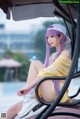 A woman with purple hair sitting on a chair by a pool.