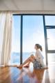 A woman sitting on the floor in front of a large window.