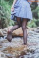 A woman in a blue and white plaid skirt is standing in a stream.