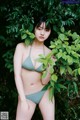 A woman in a green bikini standing in front of a bush.