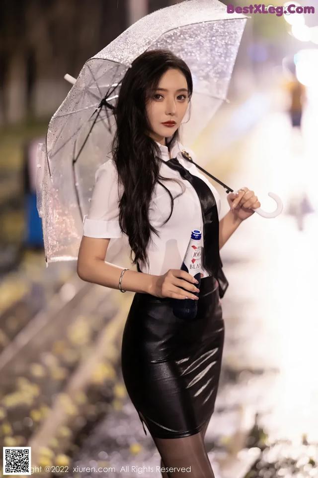A woman in a black leather skirt holding an umbrella.