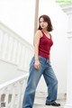 A woman in a red tank top and blue jeans posing for a picture.