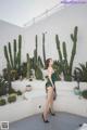 A woman in a green dress standing in front of a cactus.