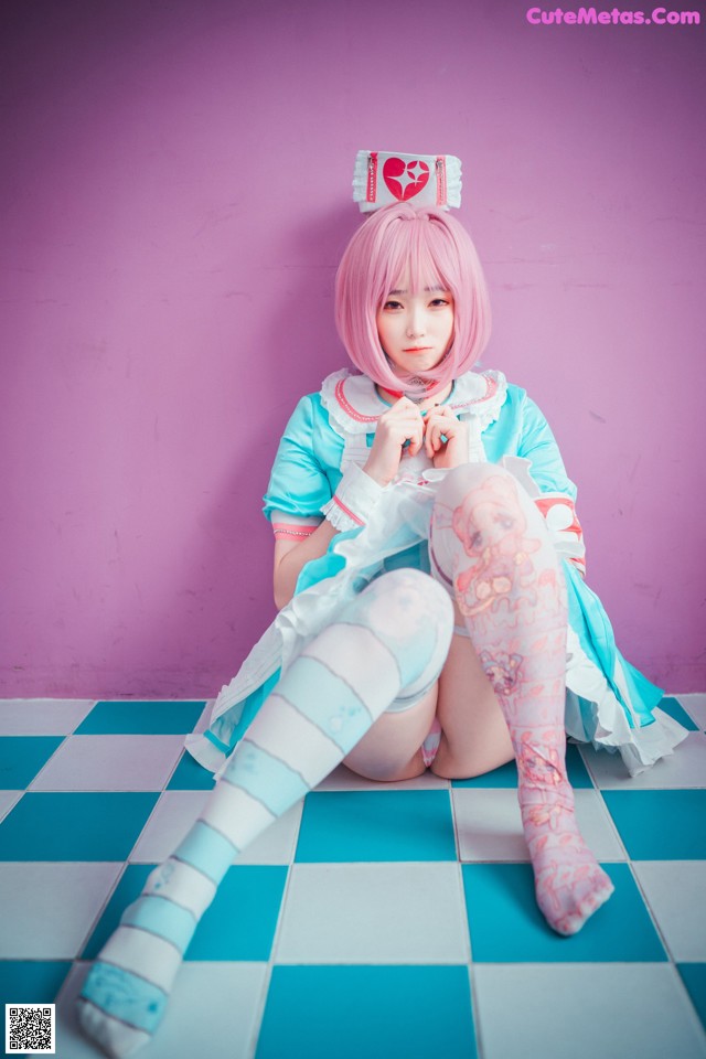 A woman with pink hair sitting on a checkered floor.