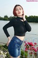A woman in a black top and denim skirt posing by the water.